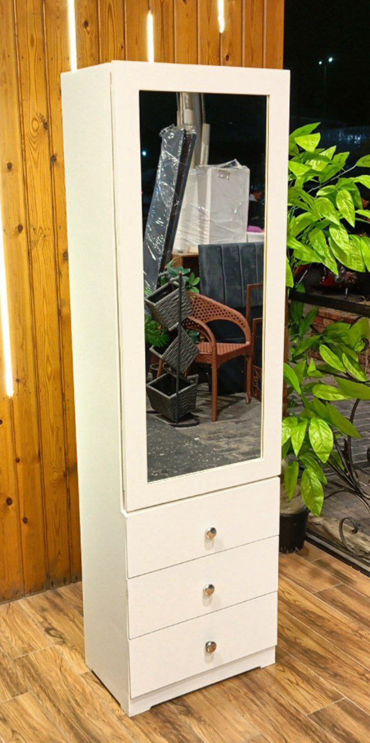 White cabinet with a mirror on a wooden floor with plants in the background